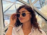 Junge Frau trägt Sonnenbrille, blau-weiß gestreiftes Hemd und eine Perlenkette.